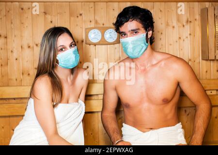 Bella coppia rilassante mentre si prende una sauna indossando maschere, concetto di coronavirus Foto Stock