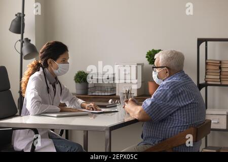 Medico femminile e paziente anziano che indossano maschere del viso che parlano Foto Stock