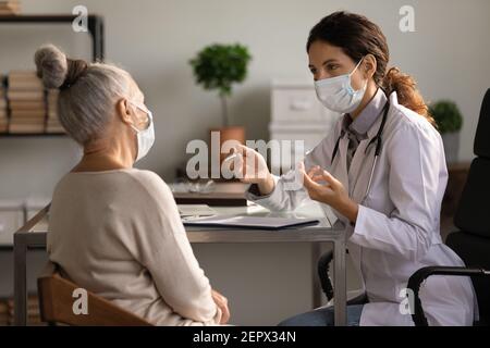 Primo piano medico serio che indossa maschera consultando paziente donna matura Foto Stock