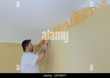 Man il processo di aggiornamento del muro rimuovendo la mano strappare la vecchia carta da parati dalla parete preparandosi per la riparazione domestica lavorare con una spatola Foto Stock