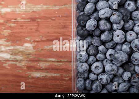 Mirtilli in un contenitore di plastica su fondo di legno. Concetto di alimentazione sana e nutrizione Foto Stock