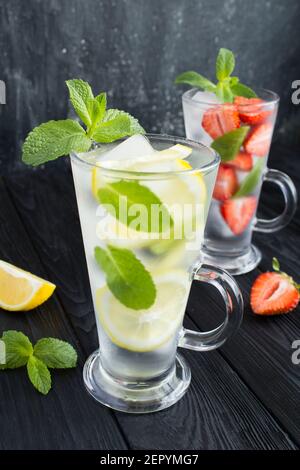 Infondere o disintossicare l'acqua con fragola, limone e menta nei due bicchieri su sfondo scuro. Primo piano. Posizione verticale. Foto Stock