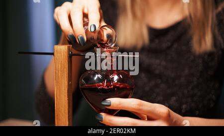 La donna strega prepara una pozione. Pozione d'amore rossa in un vaso di vetro a forma di cuore. Concetto di magia dell'amore Foto Stock