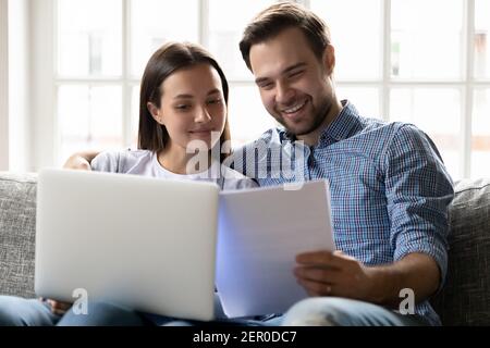 Felice coppia millennial che legge documenti finanziari su laptop Foto Stock