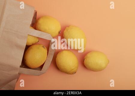 posa piatta di diversi limoni uscenti da un supermercato sacchetto di carta su sfondo arancione Foto Stock