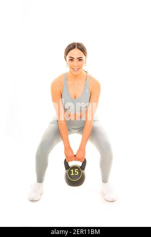 Ritratto verticale di una giovane donna che solleva un kettlebell di 15 kg mentre si fa un allenamento, isolato su uno sfondo bianco. Foto Stock