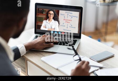 Uomo d'affari nero che lavora utilizzando il laptop sul suo posto di lavoro, avendo formazione Foto Stock