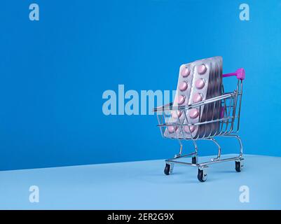 Blister di compresse rosa nel carrello del supermercato su sfondo blu con skyline alla moda inclinato e spazio di copia. Foto Stock