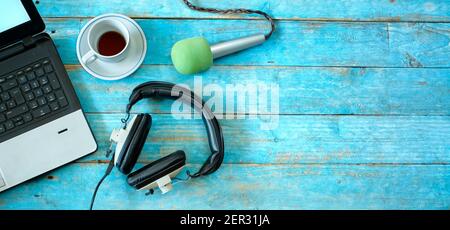 Musica, podcast o audiolibri, piatto con cuffie, microfono, caffè e laptop su tavolo di legno blu Foto Stock