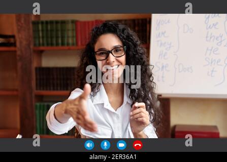 Positiva giovane donna con occhiali che si allunga la mano, avendo chiamata online Foto Stock