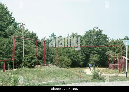 7-21-2019 Sachkhere Regione Georgia - tubi di gas sopraelevati che corrono Attraverso i villaggi della Georgia e oltre le strade - locali coppia a piedi lungo la strada laterale Foto Stock