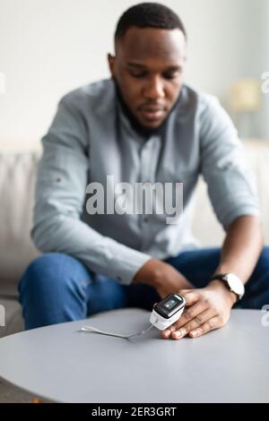 Black Man misurazione del livello di saturazione dell'ossigeno con pulsossimetro in ambienti chiusi Foto Stock