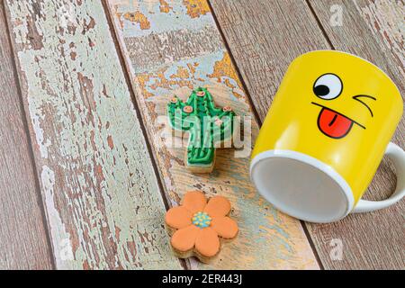 Biscotti e cactus a forma di fiore, accanto a una tazza gialla che si trova in basso (vista dall'alto). Foto Stock