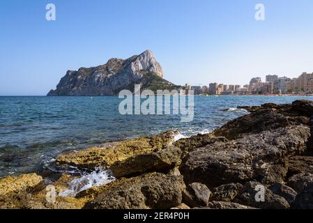 Vista dalle rocce della costa con la spiaggia urbana di Calpe e la falesia sullo sfondo, Alicante, Spagna Foto Stock