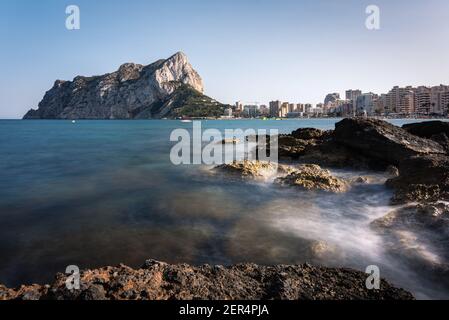 Vista dalle rocce della costa con la spiaggia urbana di Calpe e la falesia sullo sfondo, Alicante, Spagna Foto Stock