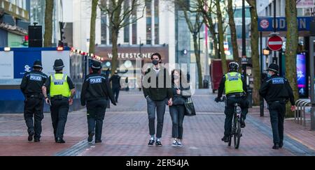 Birmingham, Regno Unito, Regno Unito. 28 febbraio 2021: Una coppia mascherata cammina di mano in mano lungo New Street come una maggiore presenza della polizia può essere visto attraverso la città, come parte del Project Servator (lotta contro il crimine dei coltelli e il terrorismo) e di polizia le restrizioni COVID. Credit: Ryan Underwood / Alamy Live News Foto Stock