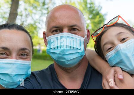 Famiglia in maschere mediche protettive. Madre, padre, figlia si proteggono dal virus Coronavirus. Famiglia in maschere mediche all'aperto. Primo piano Foto Stock