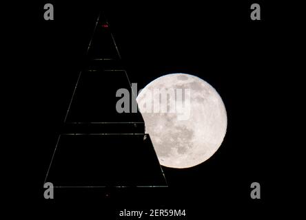 28 febbraio 2021, Hessen, Francoforte sul meno: La luna piena è sopra la cima del Messeturm a Francoforte. Le temperature scendono di nuovo sotto il congelamento, specialmente di notte. Foto: Boris Roessler/dpa Foto Stock