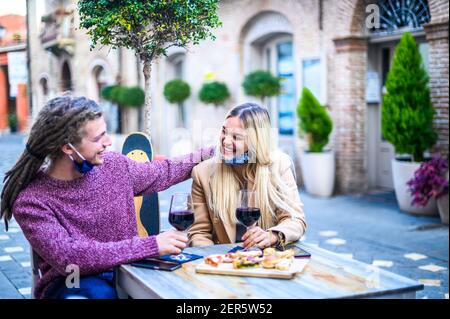 Giovane coppia innamorato bere vino rosso con maschera facciale Nella piazza in pandemia tempo-felice millennial persone a. Ristorante godendo del tempo aperitivo - NE Foto Stock