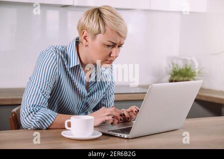 Donna seria messa a fuoco che lavora sul laptop a casa femmina che usa computer portatile in cucina Foto Stock