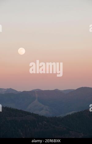 Panoramica luna piena sopra le cime delle montagne con tramonto cielo arancione. Foto Stock