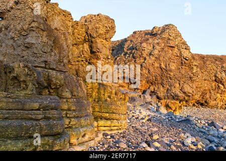 La luce del sole dorata del mattino presto illumina le scogliere e gli affioramenti calcarei a Trow Rocks sulla costa del Mare del Nord a South Shields in Tyne and Wear. Foto Stock