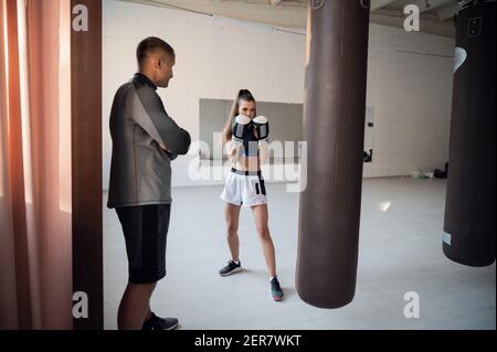 Donna che addestra pugilato con personal trainer. Istruttore che insegna pratica di combattimento pugile femminile insieme Foto Stock