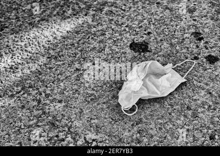 Grintosa resa in bianco e nero di una maschera facciale su strada asfaltata. Per Covid UK, non indossare maschere facciali, reazione alla maschera americana mandato da Biden. Foto Stock