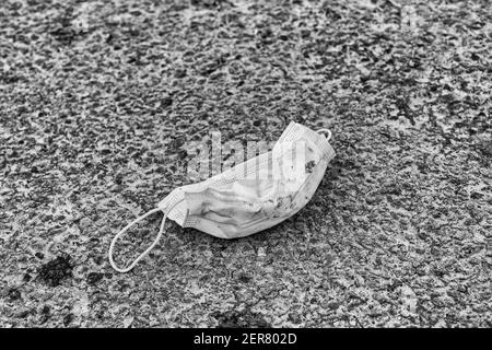 Grintosa resa in bianco e nero di una maschera facciale su strada asfaltata. Per Covid UK, non indossare maschere facciali, reazione alla maschera americana mandato da Biden. Foto Stock