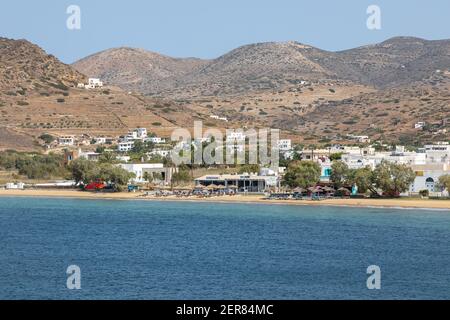Chora, Isola di iOS, Grecia - 26 settembre 2020: Vista della spiaggia sabbiosa sull'isola greca di iOS lettini e ombrelloni. Città sullo sfondo. Giorno nuvoloso Foto Stock