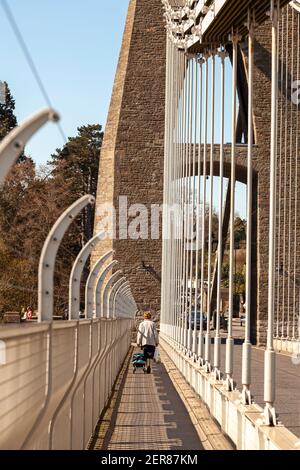 Bristol, UK 04-17-2010: Una donna anziana cammina da sola con borse per lo shopping sul sentiero del Clifton Suspension Bridge che corre sul fiume Avon Foto Stock