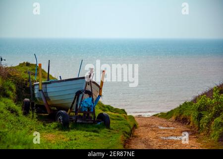 Una piccola barca di legno è lasciata su un carro trainante da un sentiero sterrato vicino all'oceano. La strada conduce ad una piccola rampa di accesso. L'immagine è stata presa su un hikin di prateria Foto Stock