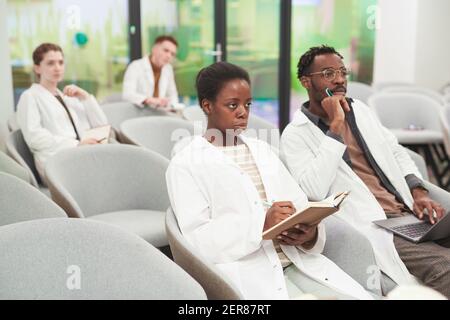 Ritratto di donna afroamericana seduta in udienza con gruppo multietnico di persone mentre ascoltano la lezione sulla medicina, copia spazio Foto Stock