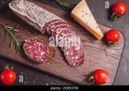 Salsiccia di prosciutto affumicata e fette tagliate con rosmarino e ciliegia pomodori su tavola di legno scuro Foto Stock