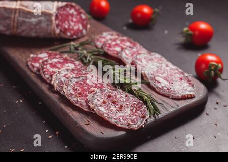 Salsiccia di prosciutto affumicata e fette tagliate con rosmarino e ciliegia pomodori su tavola di legno scuro Foto Stock