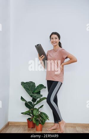 Donna incinta spensierata al club di yoga, tenendo il tappetino arrotolato, in posa per una foto Foto Stock