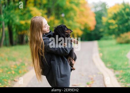 Donna abbracciando cane nel parco estivo. Signora allegra con lunghi capelli scuri abbracci e colpi amichevole vecchio cane seduta su prato verde lussureggiante di garde pubblica Foto Stock