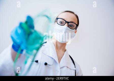 Medico con occhiali e guanti protettivi mette su maschera di ossigeno. Foto Stock