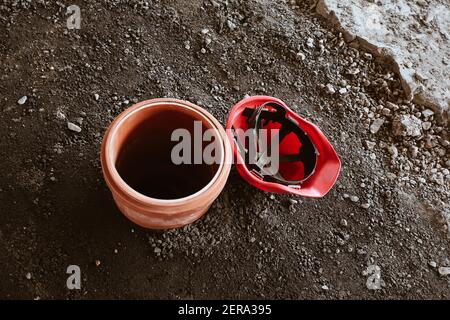 Costruzione edificio sito di sfondo con tubo di plastica in terra per base colonnare e casco rosso sulla superficie delle pietre arrossate Foto Stock