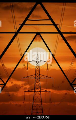 Elettricità Pylon o Torre elettrica al tramonto con cielo arancione. La bellezza industriale nel paesaggio come i cavi trasportano l'elettricità intorno al paese Foto Stock