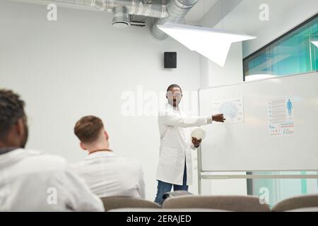 Vista grandangolare dell'uomo afroamericano in piedi da lavagna mentre si dà seminario sulla medicina al college, spazio copia Foto Stock