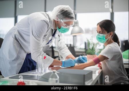 In una clinica privata infermiere un uomo mette un tourniquet sul braccio di una paziente femmina e prende il sangue da una vena per l'analisi Foto Stock