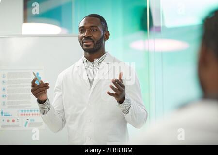 Vita in su ritratto di afroamericano uomo in piedi da lavagna mentre dà la presentazione durante il seminario medico all'università, spazio di copia Foto Stock