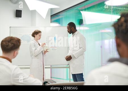 Vista laterale ritratto di giovane donna in piedi da lavagna mentre dà la presentazione durante il seminario medico in università, spazio di copia Foto Stock