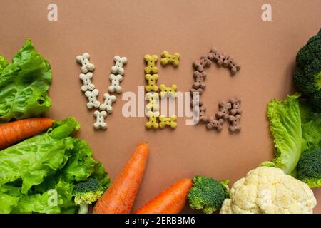 Croccini secchi vegetariani del cane in forma di osso con verdure su sfondo beige. VENG. Scritta Foto Stock