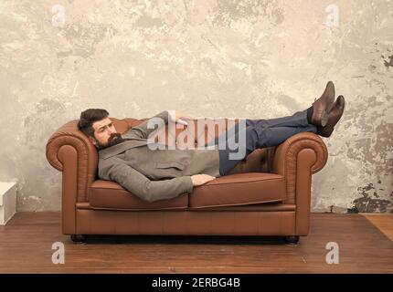 Aspetto bello e soggiorno di moda. Brutale hipster rilassarsi sul divano. Uomo bearded con look di moda. Moda e stile uomo. Abbigliamento casual per affari. Negozio di abbigliamento da uomo. Moda unica come voi. Foto Stock