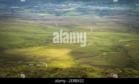 Vista dalla cima della montagna sul tortuoso sentiero in legno del lungomare di Cuilcagh Park illuminato dalla luce del sole nella valle sottostante, Irlanda del Nord Foto Stock