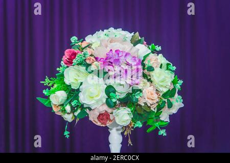 L'elemento della decorazione di nozze è un bouquet di fiori artificiali di rose all'interno della stanza sullo sfondo della tenda viola. Foto Stock