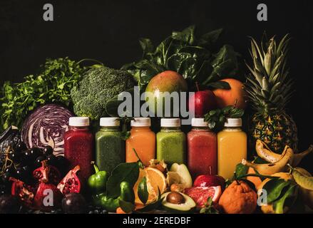 Varietà di smoothies fresco o succhi per disintossicare la dieta di perdita di peso. Succhi colorati in bottiglie con frutta, verdure e verdi intorno, sfondo scuro. Foto Stock