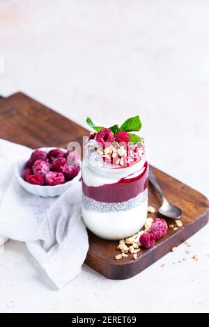 Marmellata di lamponi, budino di chia e yogurt. Condito con granola per fare un parfait in un vaso di vetro. Foto Stock